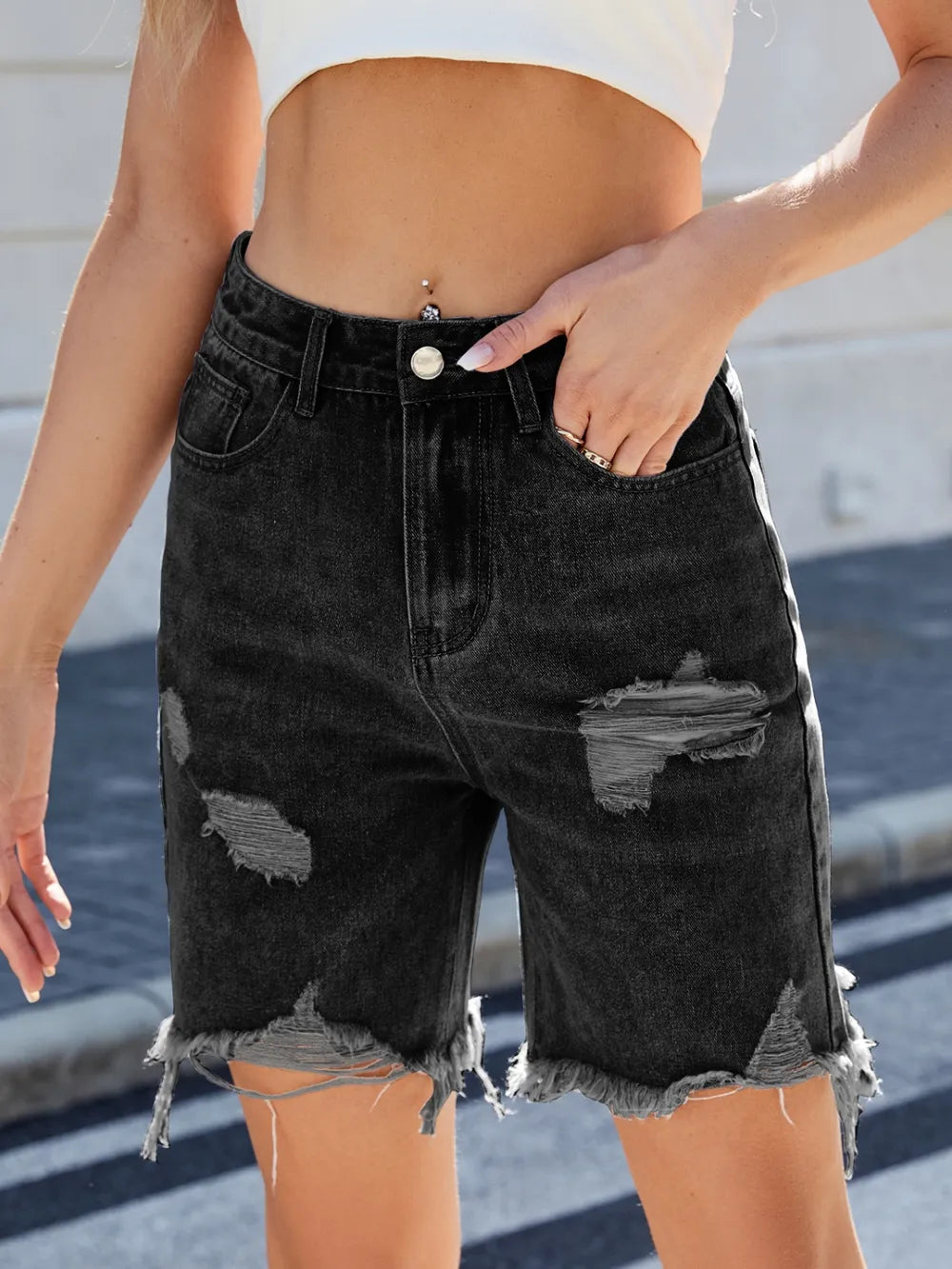 Person wearing black distressed denim shorts with a blurred background