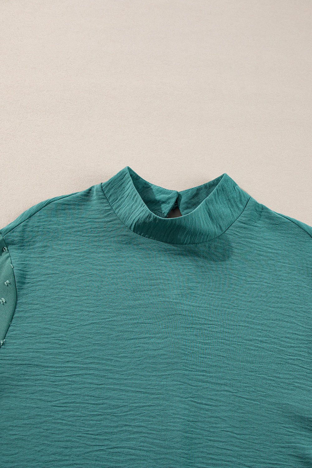 Teal shirt with a high collar on a beige background