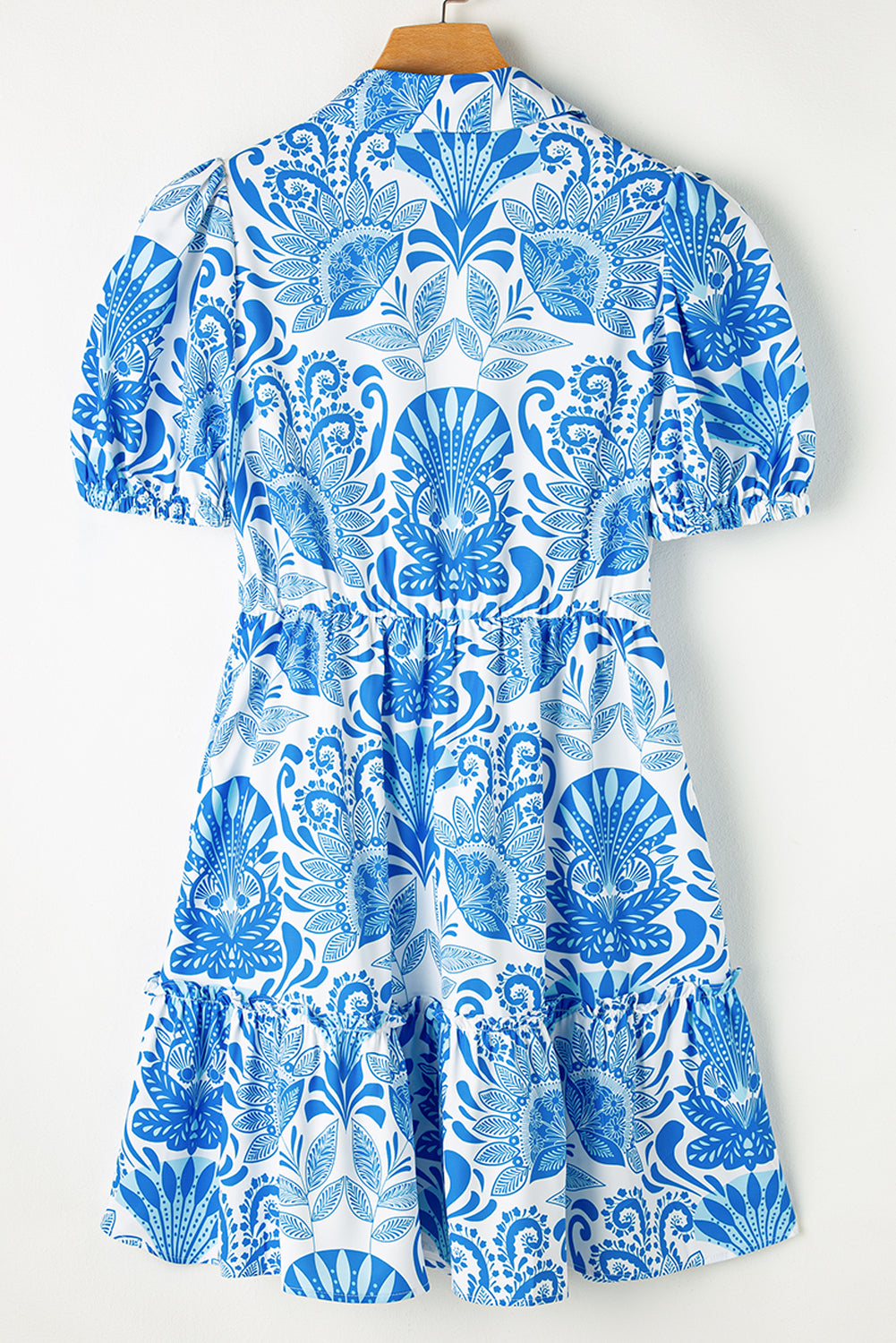 Blue and white patterned dress on a wooden hanger against a white background