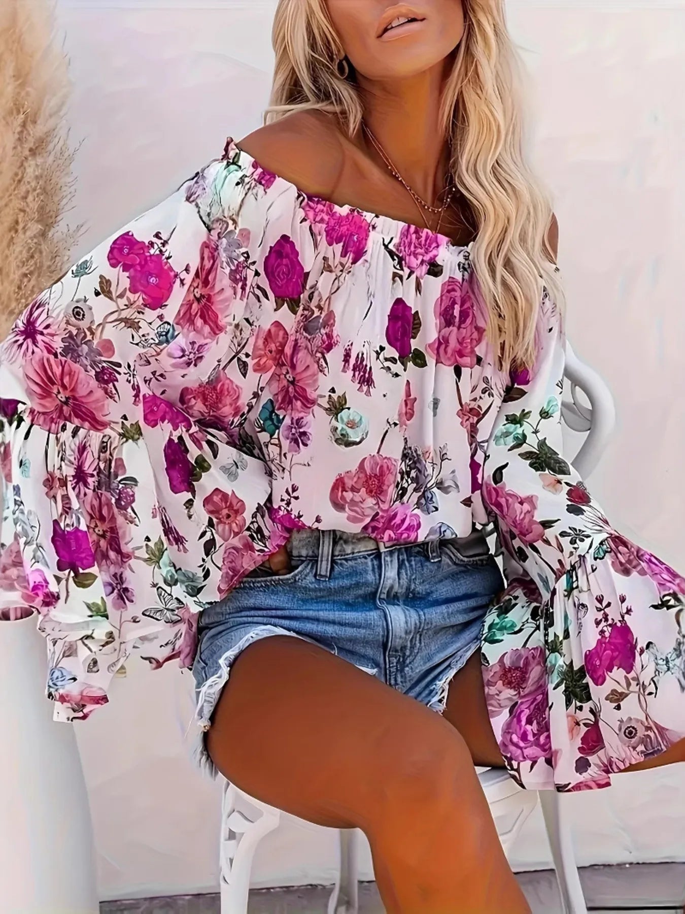 Woman wearing a floral off-shoulder top and denim shorts sitting on a chair.