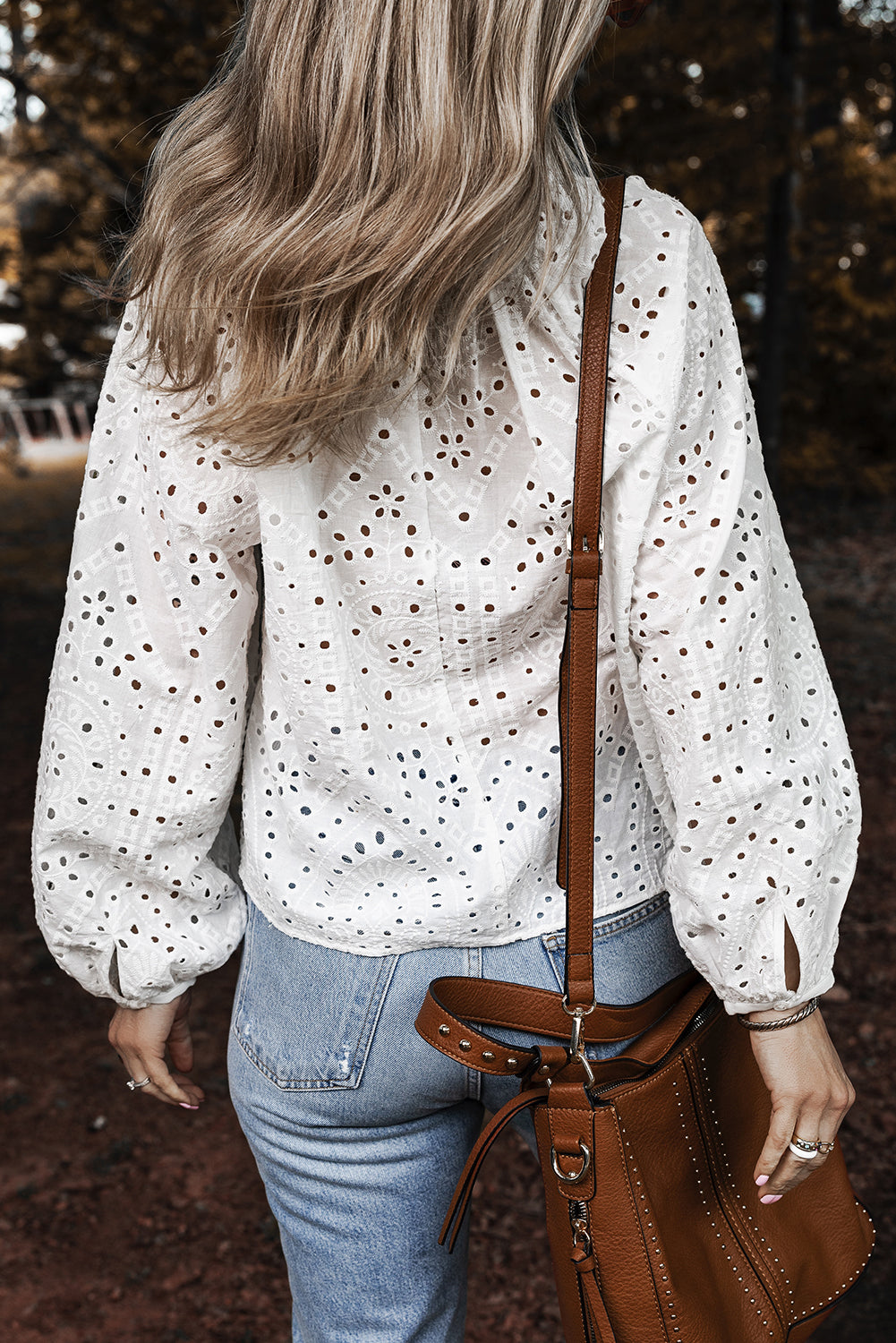 Person wearing a white blouse with black polka dots and blue jeans, holding a brown leather bag.