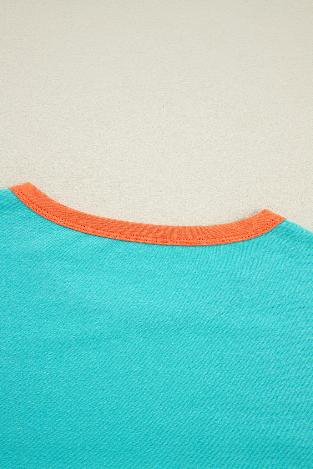 Close-up of a turquoise shirt with orange trim on a beige background