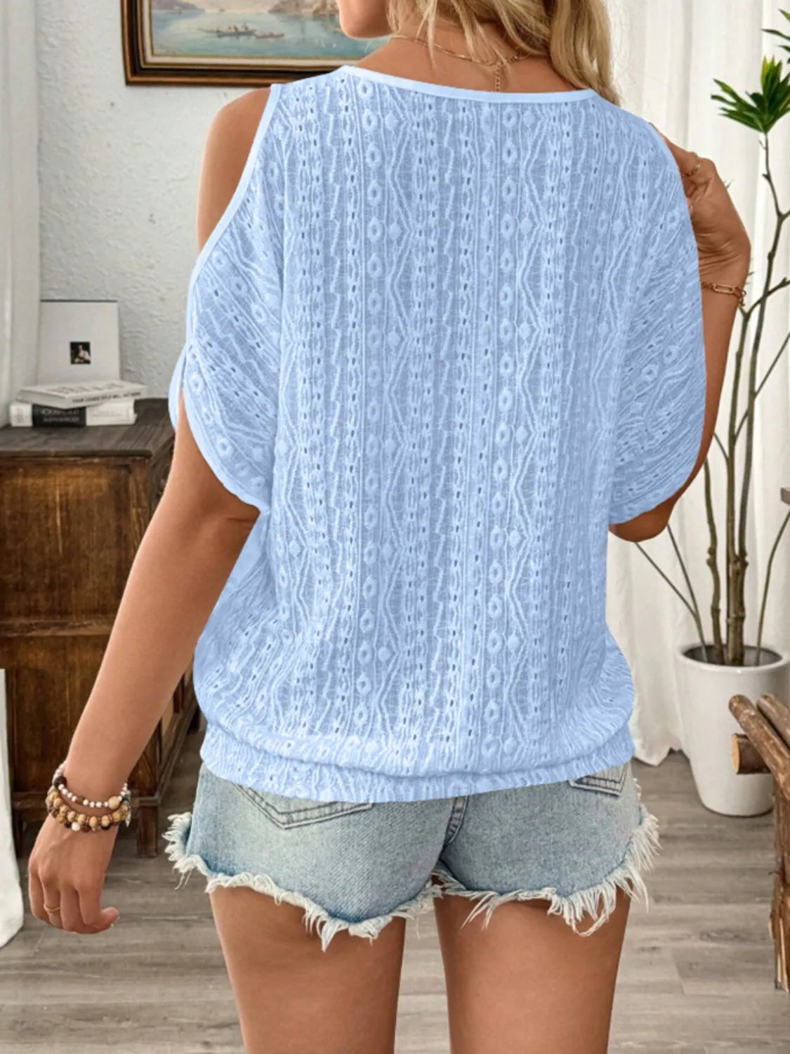 Person wearing a light blue textured top and denim shorts indoors.