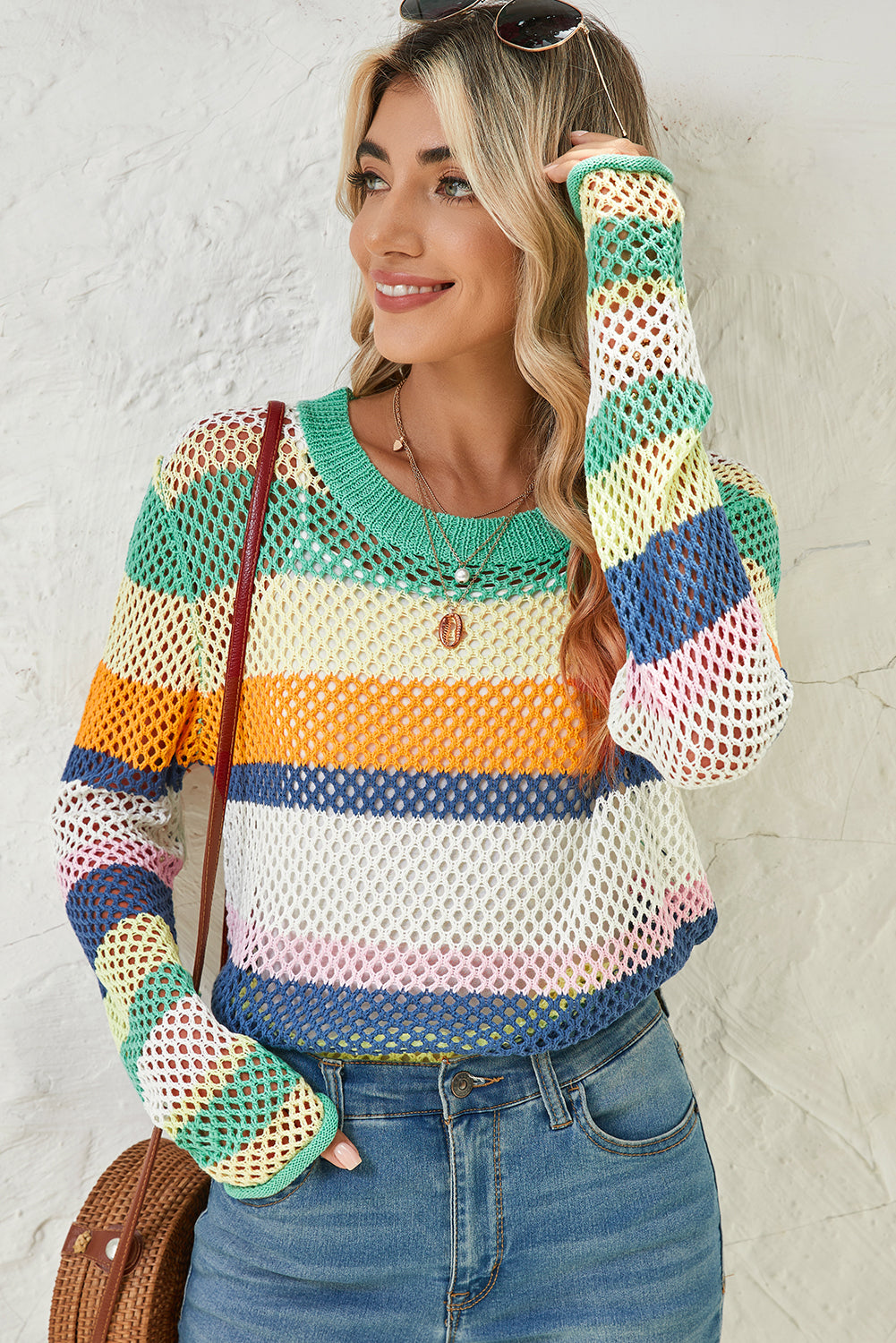 Woman wearing a colorful striped sweater and gloves against a white wall.