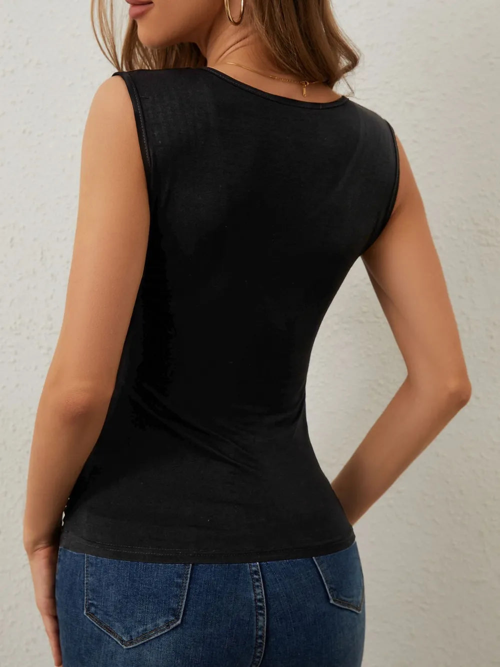 Person wearing a black sleeveless top and blue jeans against a neutral background