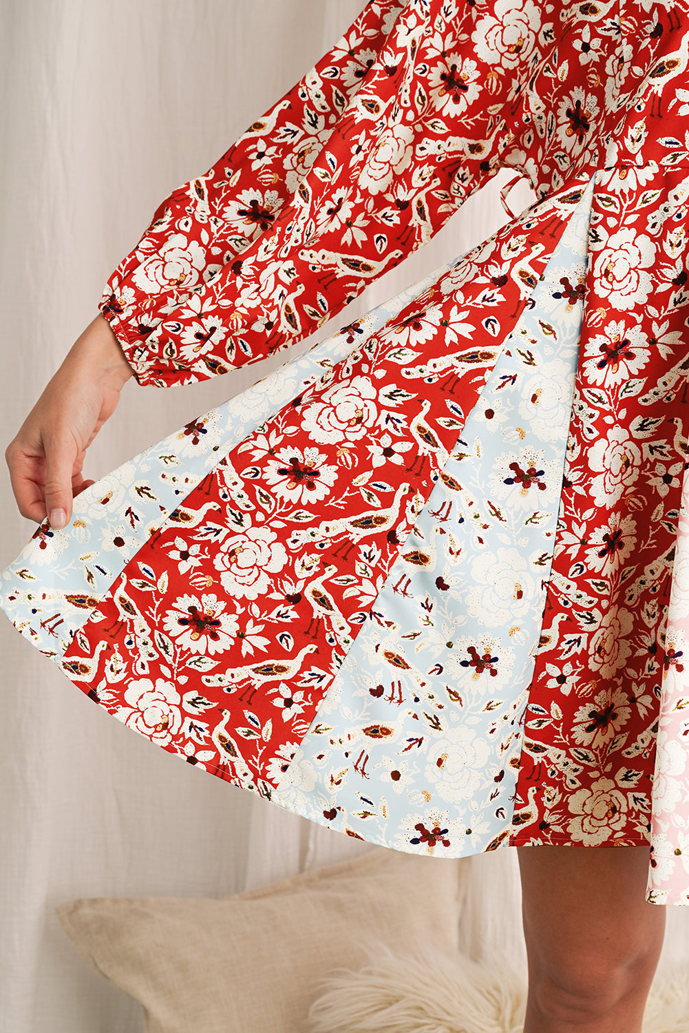Red floral dress with white lace trim held by a person against a neutral background