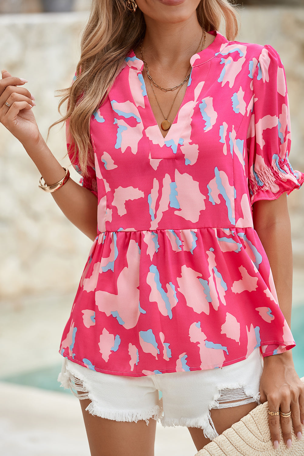 Woman wearing a pink floral blouse with white shorts by a pool.