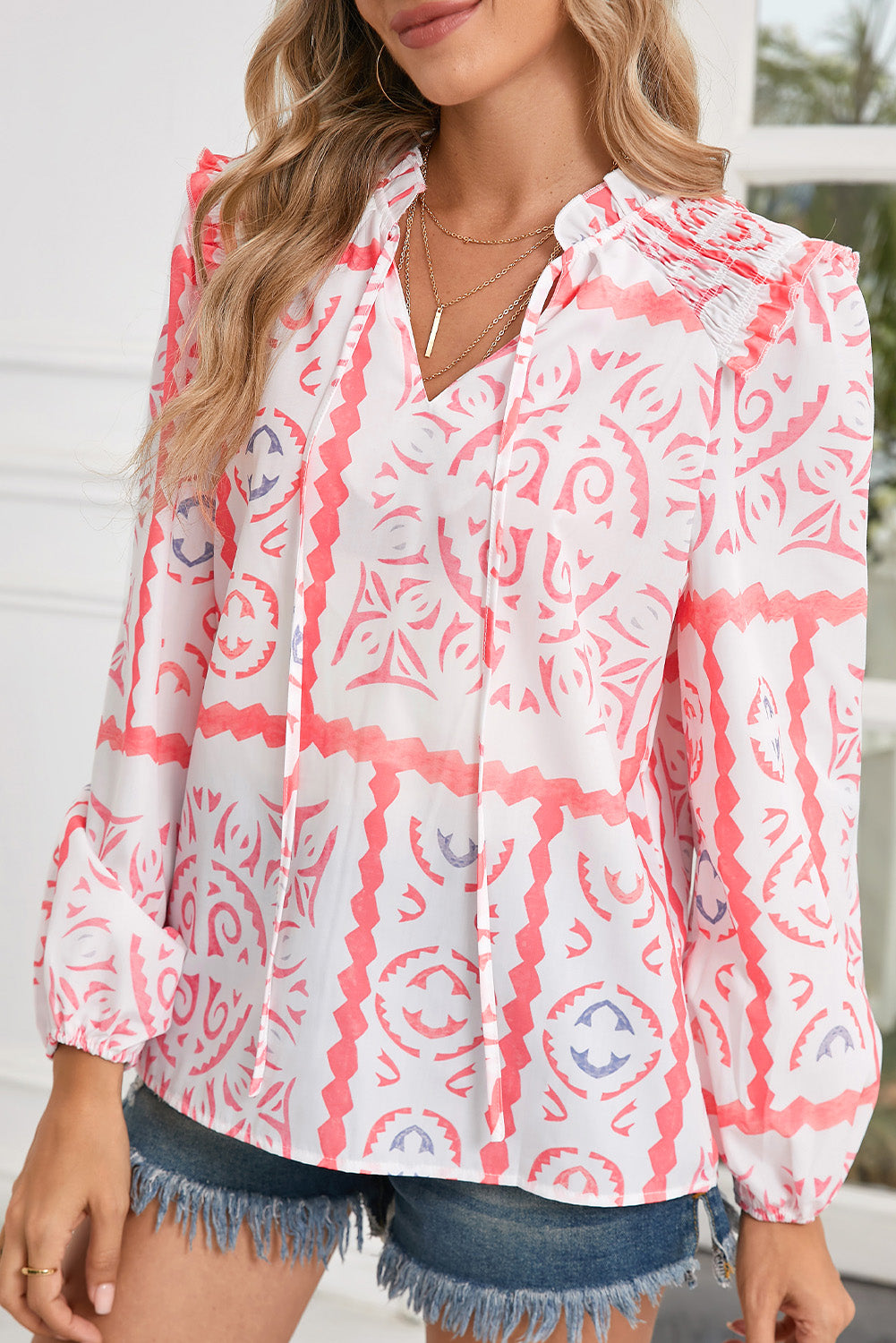 Woman wearing a pink and white patterned blouse with denim shorts.