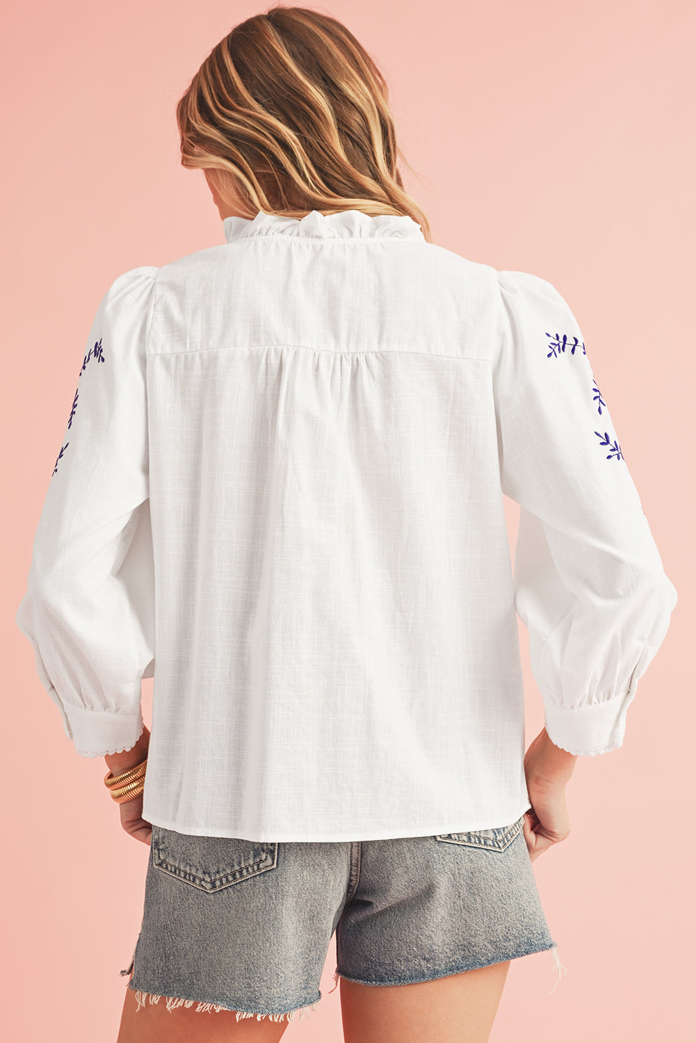 White embroidered blouse worn by a person on a pink background