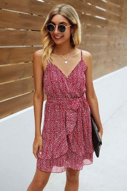 Woman wearing a pink floral dress with sunglasses against a wooden wall.