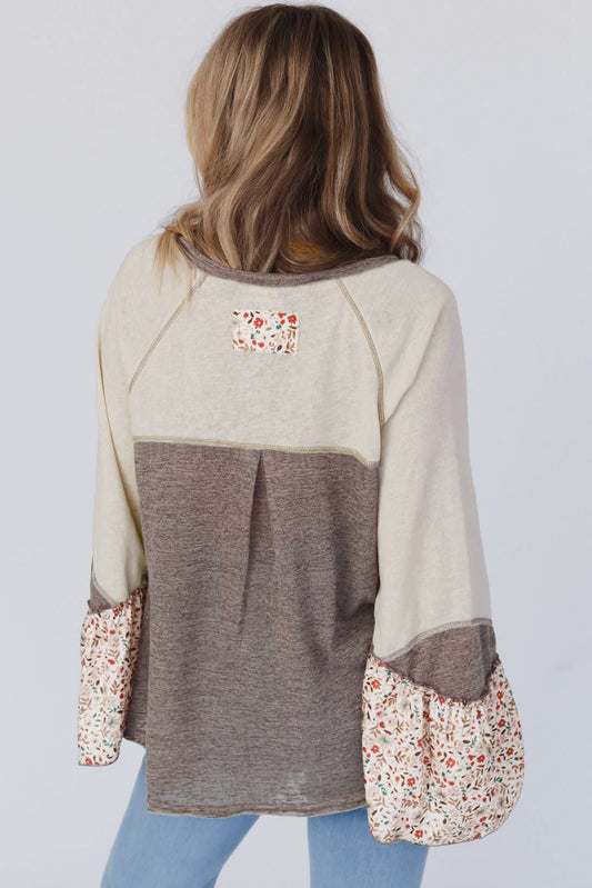 Person wearing a beige and brown sweater with floral cuffs and hem on a white background