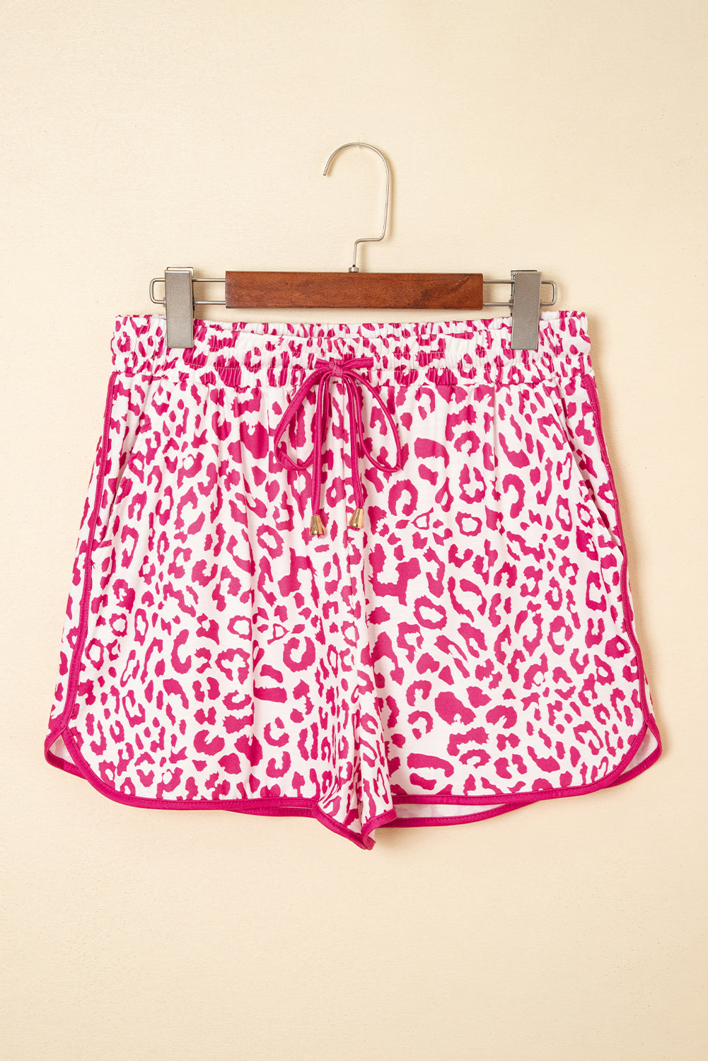 Pink leopard print shorts on a hanger against a beige background