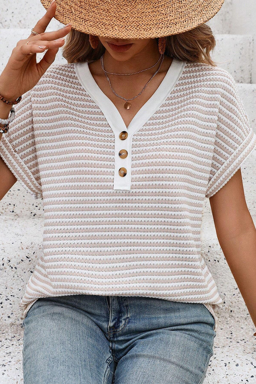 Woman wearing a textured white top with buttons and blue jeans, sitting on a textured surface.