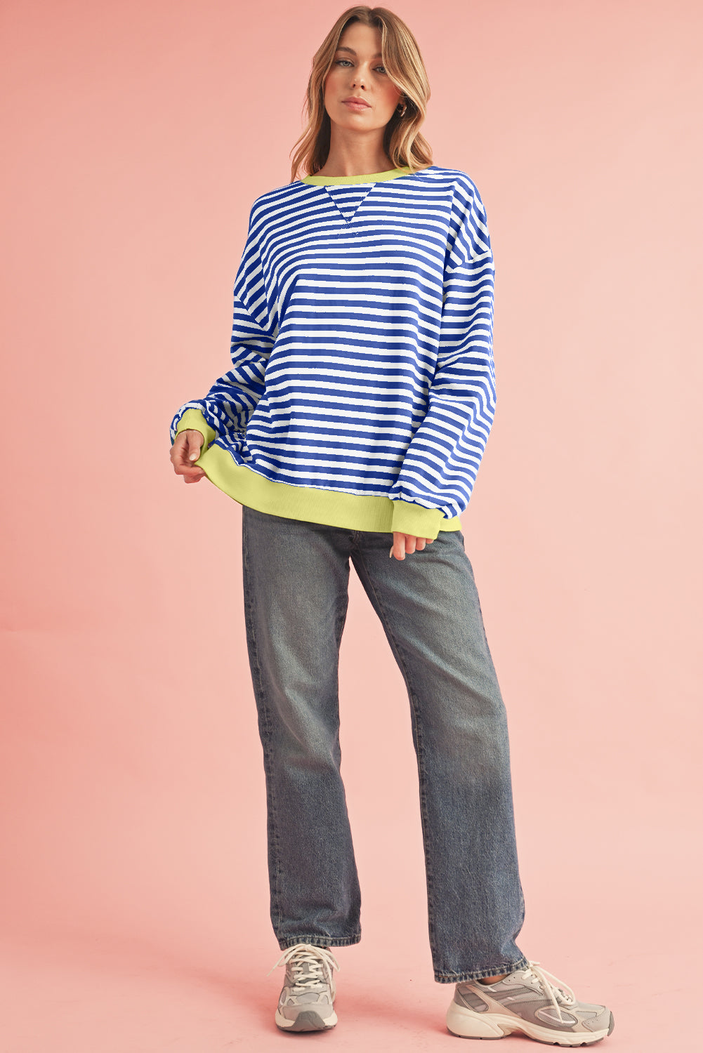 Woman wearing a blue and white striped sweater with green accents on a pink background