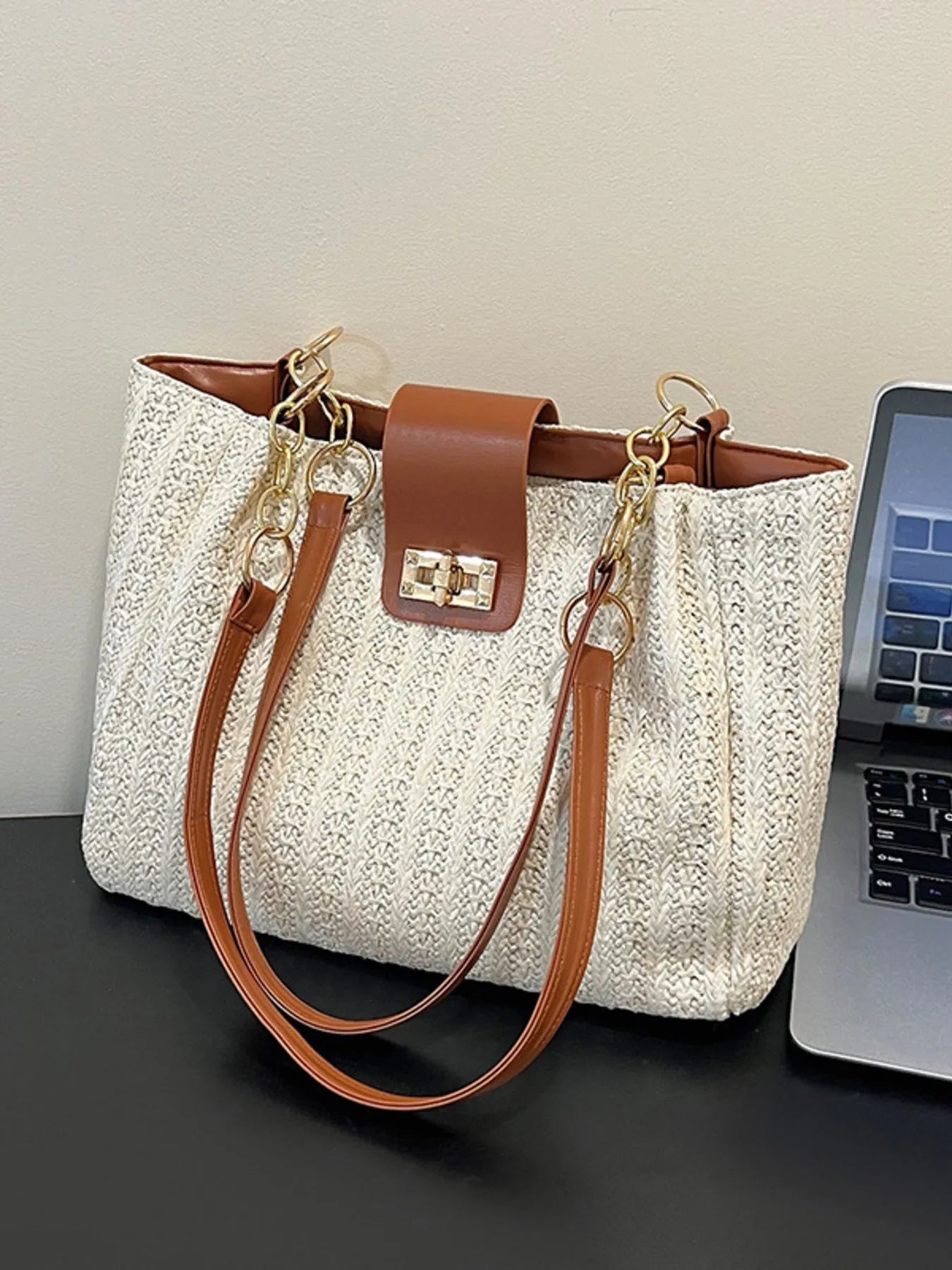 White textured handbag with brown handle and strap next to a laptop on a dark surface.