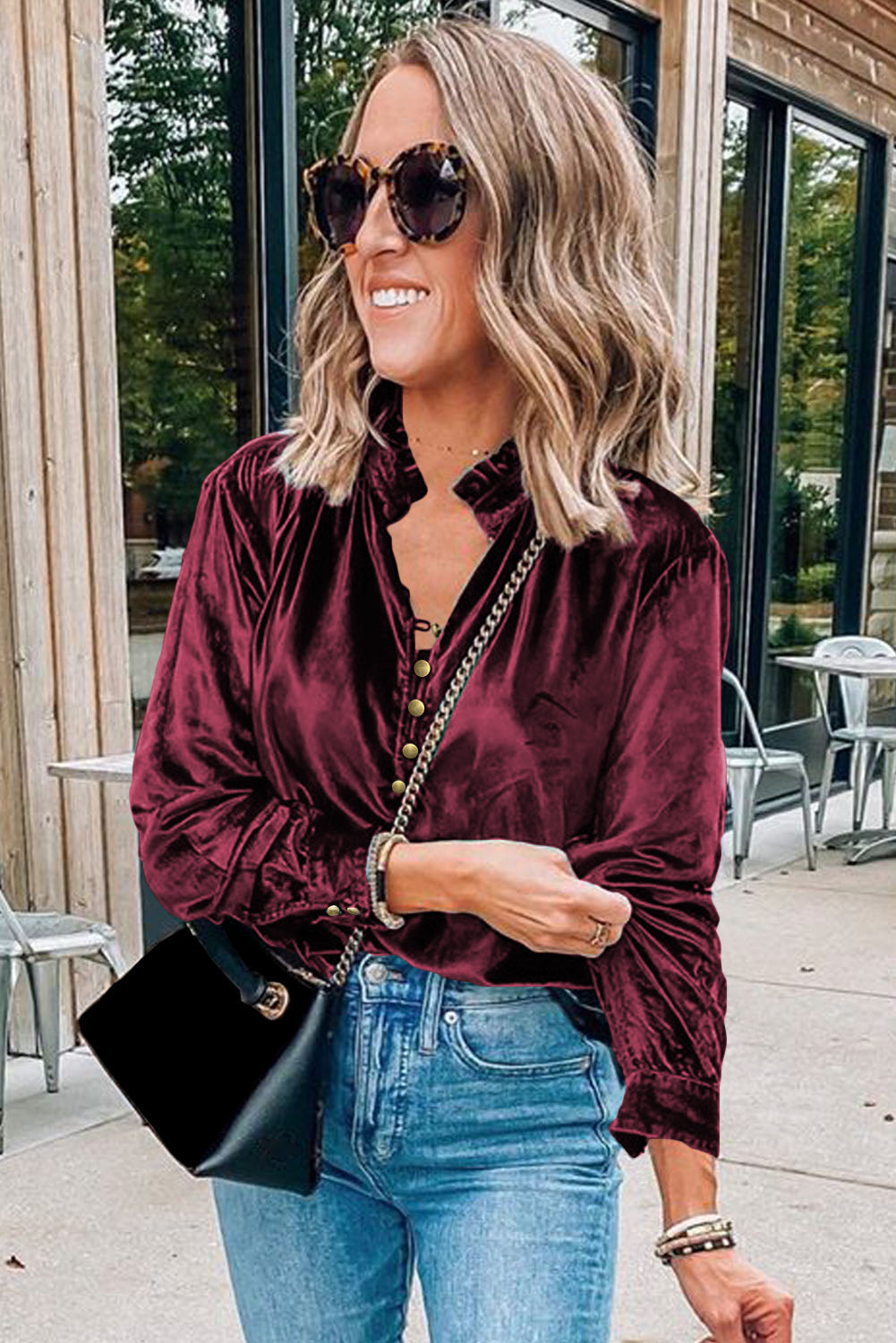 Woman wearing a burgundy velvet blouse and blue jeans outdoors.