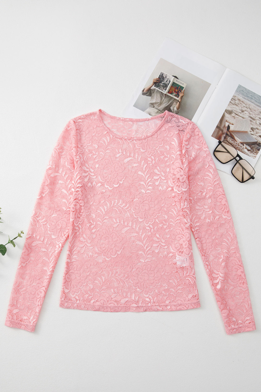Pink lace long-sleeve top on a white surface with a magazine and glasses in the background.