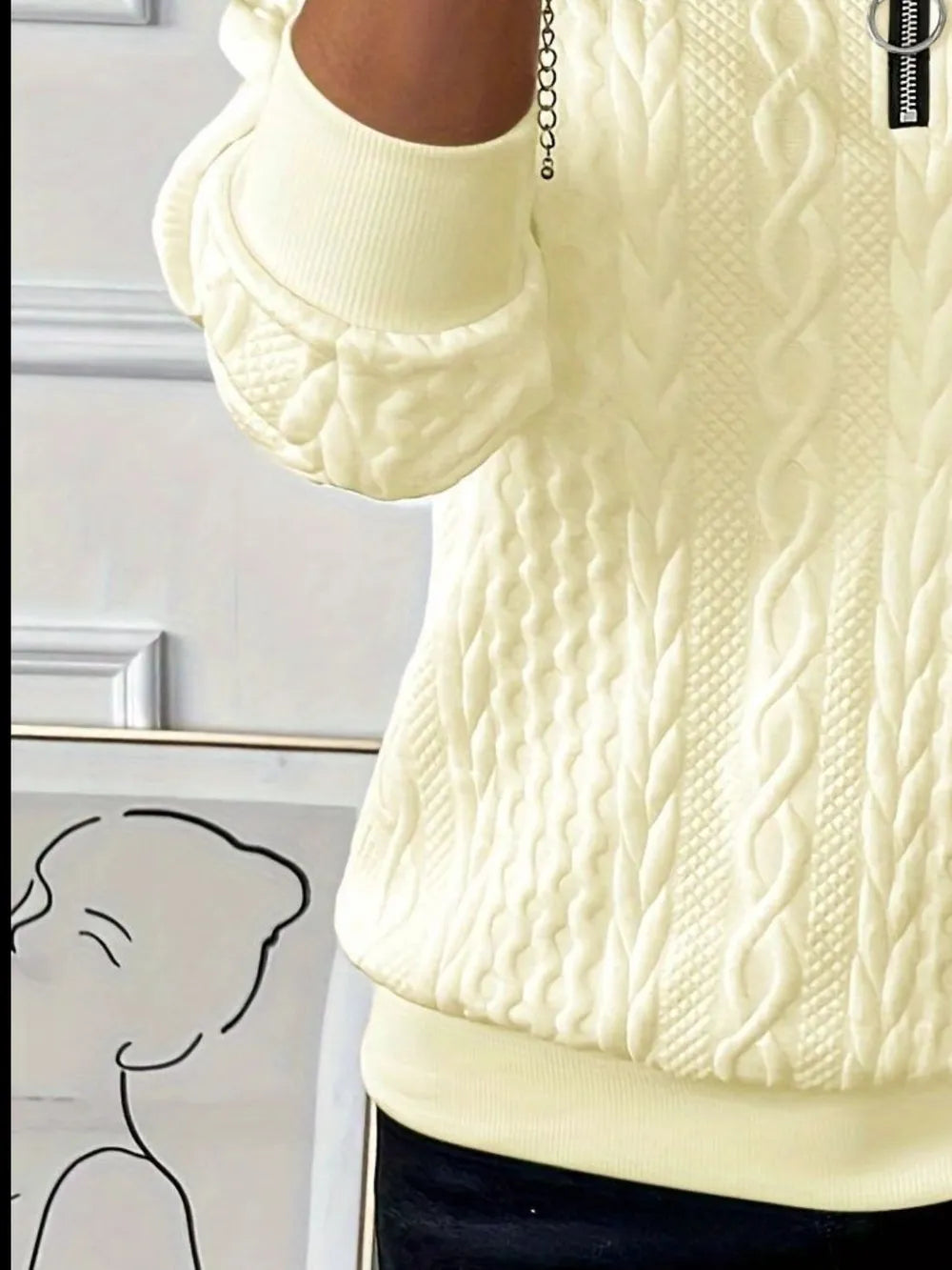 Close-up of a cream-colored cable knit sweater with a brand tag.
