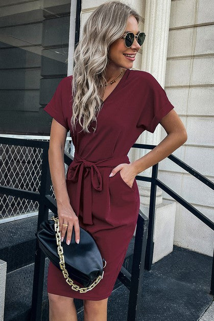 Woman in a burgundy dress standing outdoors on a city street.