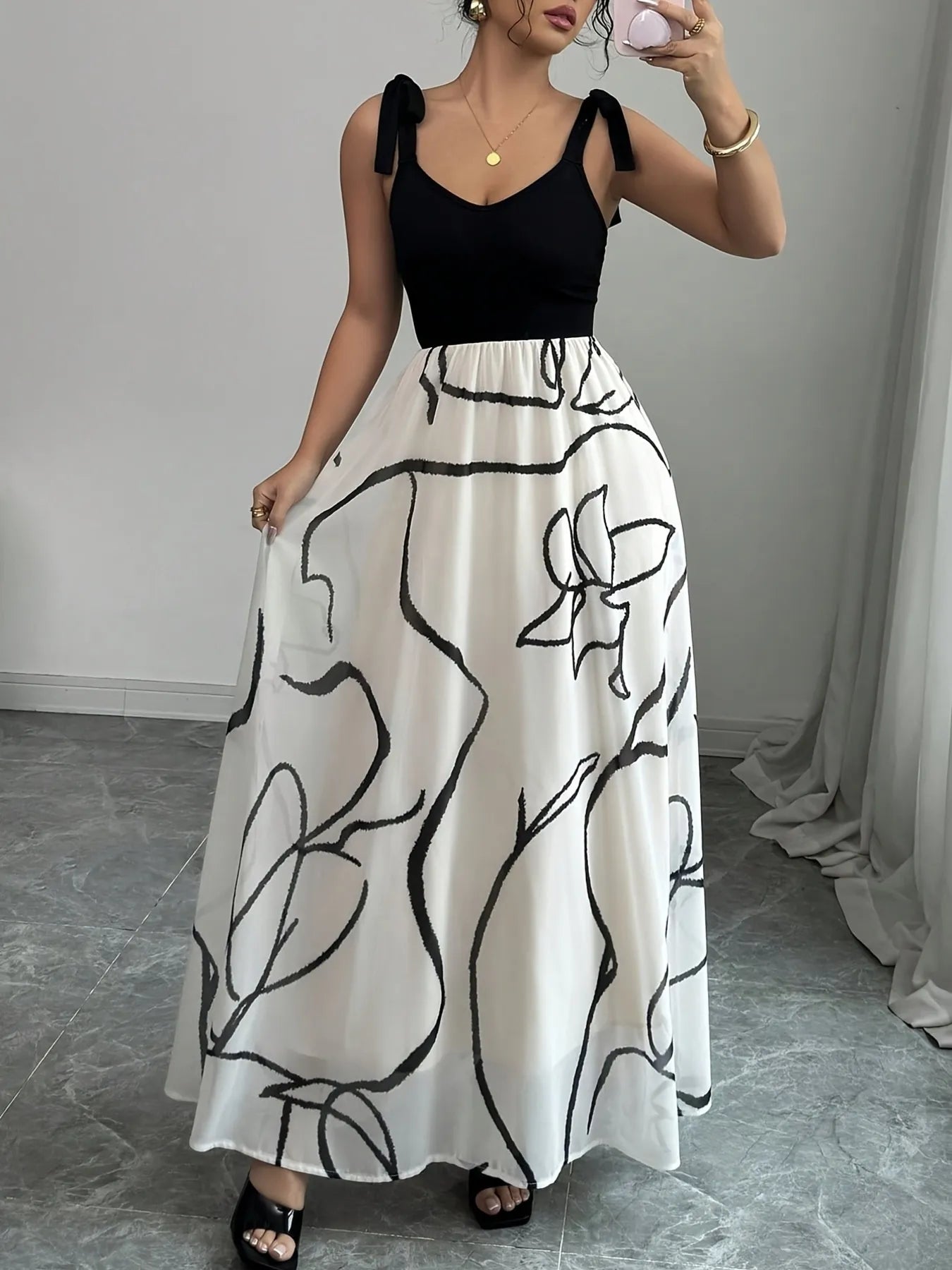 Woman wearing a black top and white skirt with black abstract patterns, standing against a plain background.