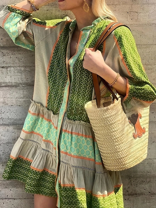 Woman wearing a green and beige patterned dress holding a straw bag against a concrete wall.