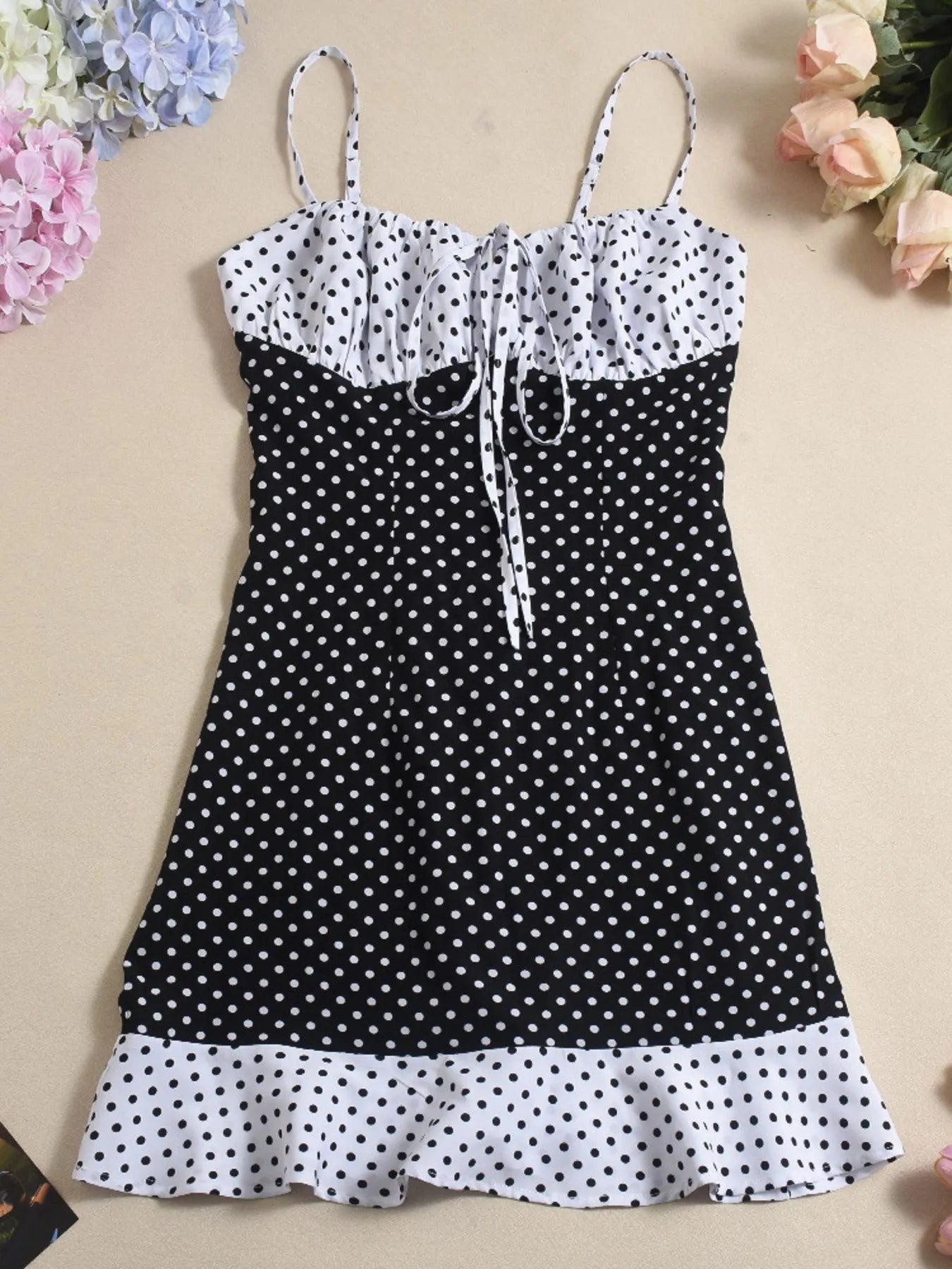 Black and white polka dot dress on a beige background with flowers around