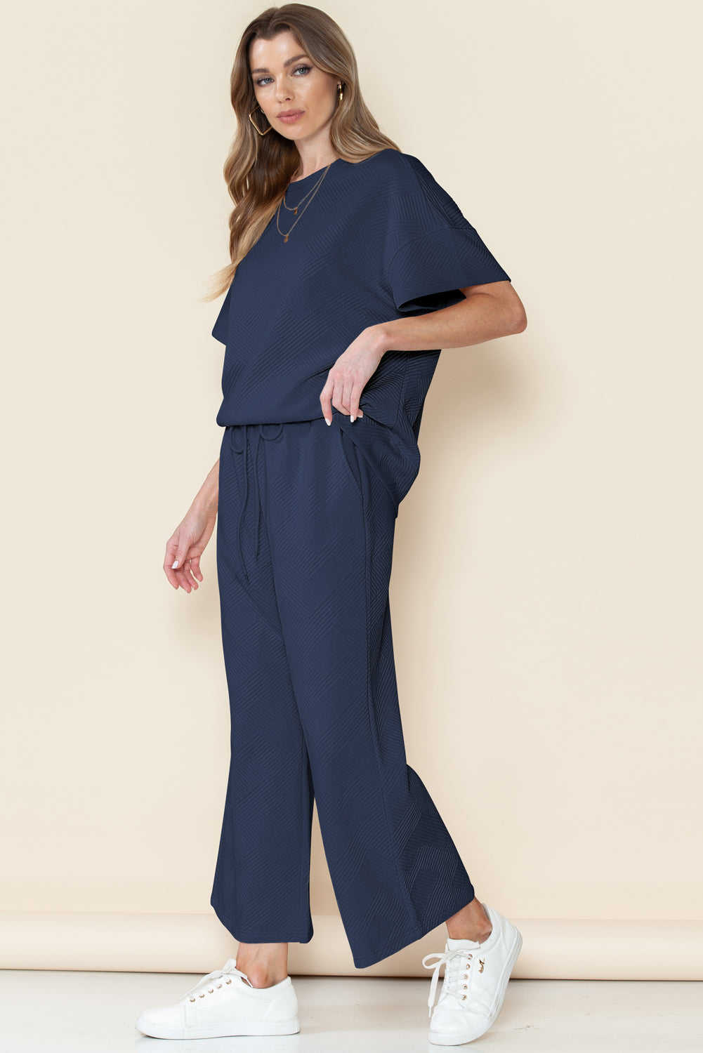 Woman wearing a navy blue outfit with white sneakers on a beige background