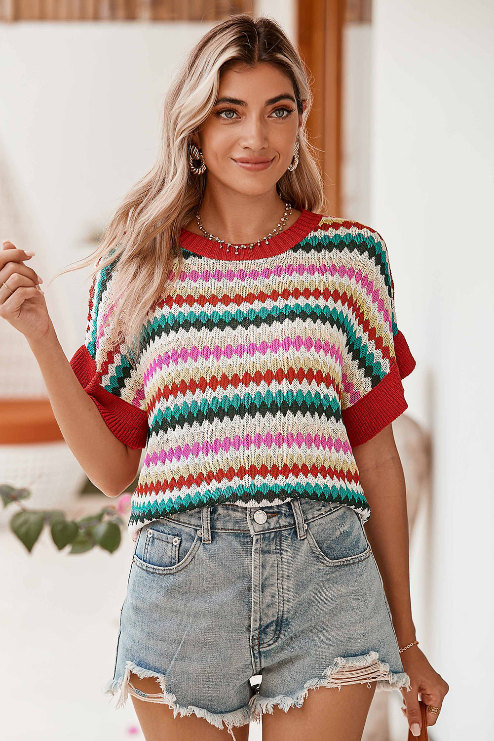 Woman wearing a colorful striped sweater and denim shorts indoors.