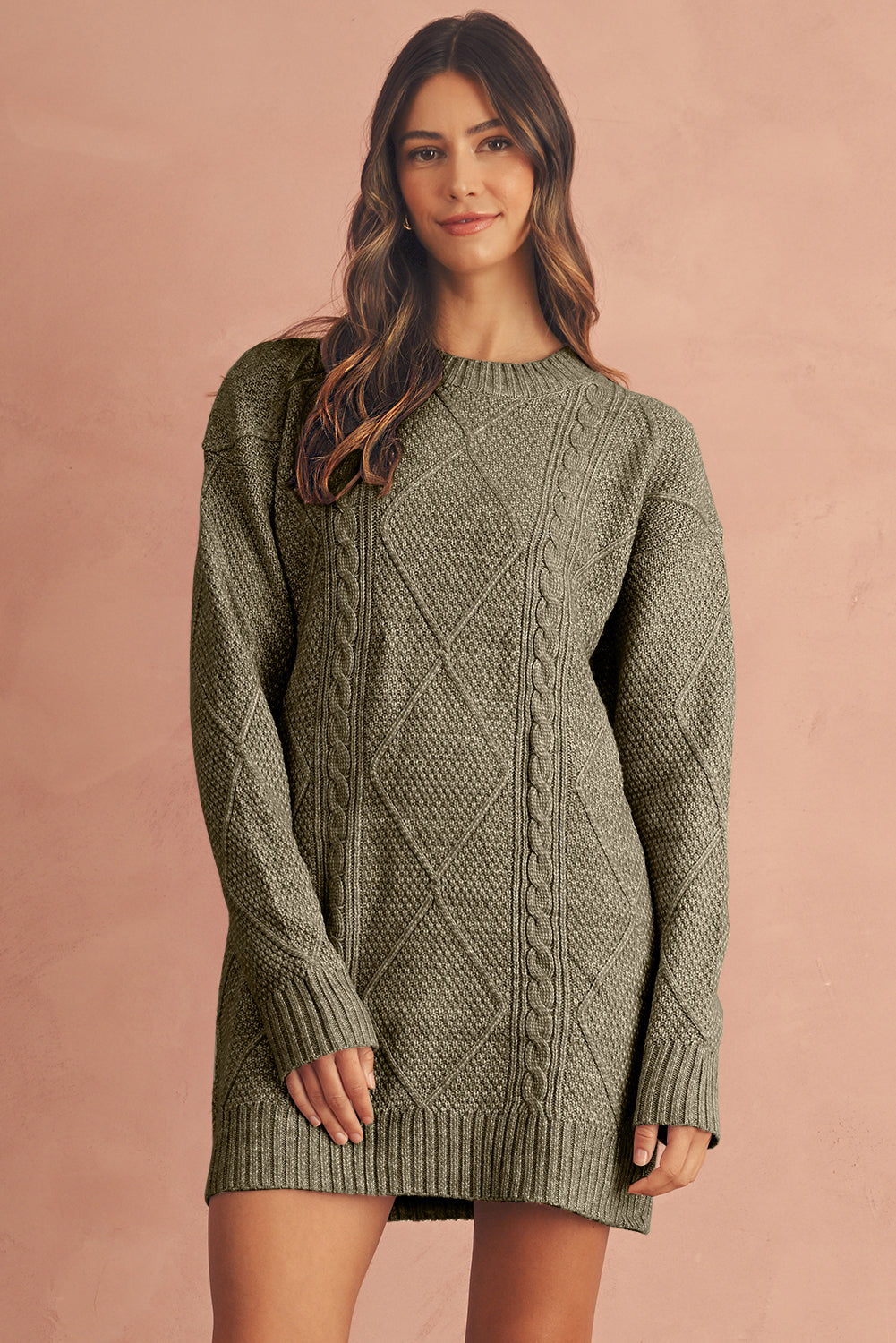Woman wearing a green cable knit sweater dress against a pink background