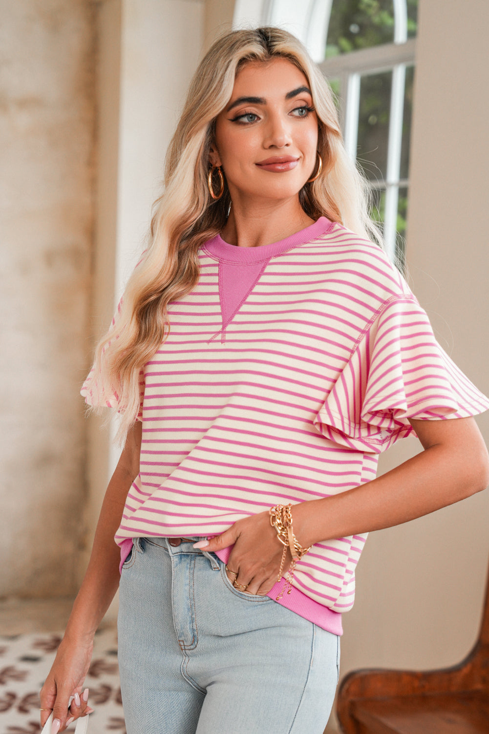 Woman wearing a pink and white striped shirt with light blue jeans indoors.