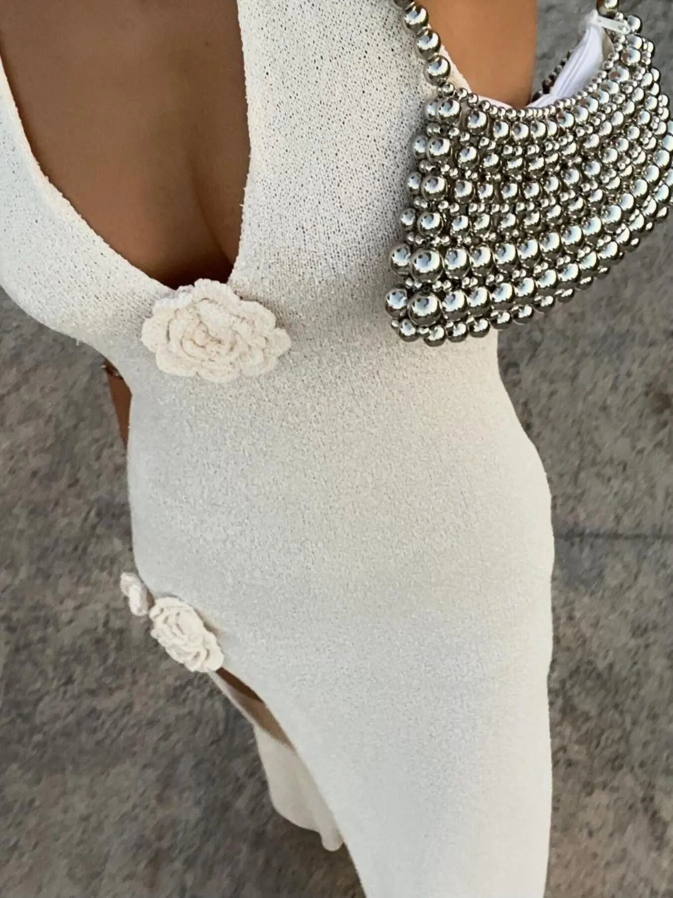 Close-up of a white dress with floral details and a beaded necklace on a neutral background