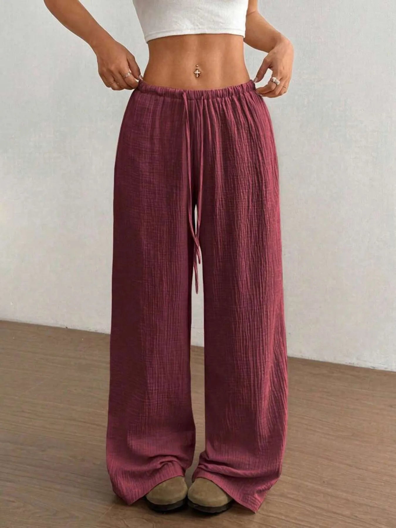 Person wearing maroon wide-leg pants with a white top against a neutral background