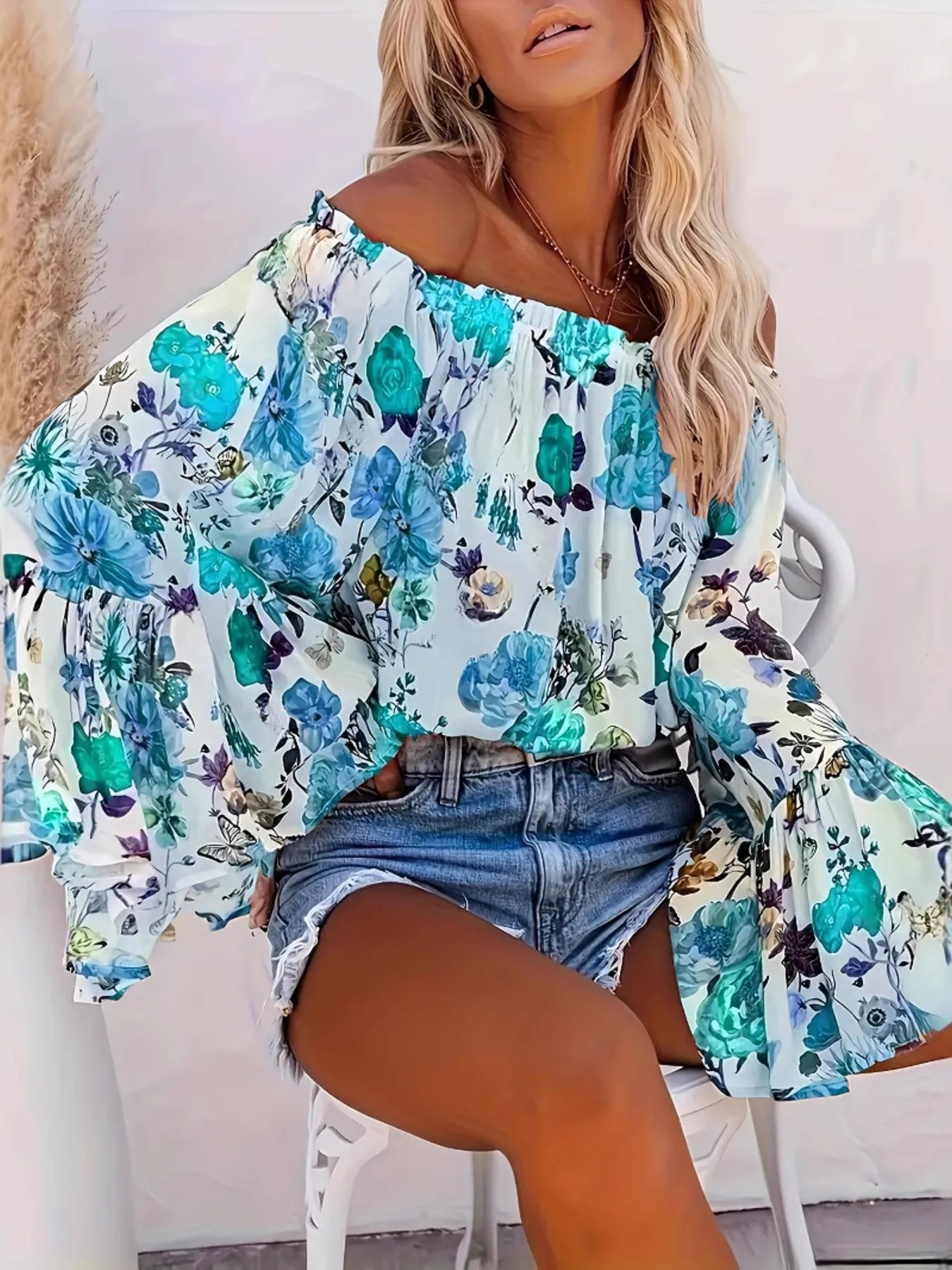 Woman wearing a floral off-shoulder top and denim shorts against a white background