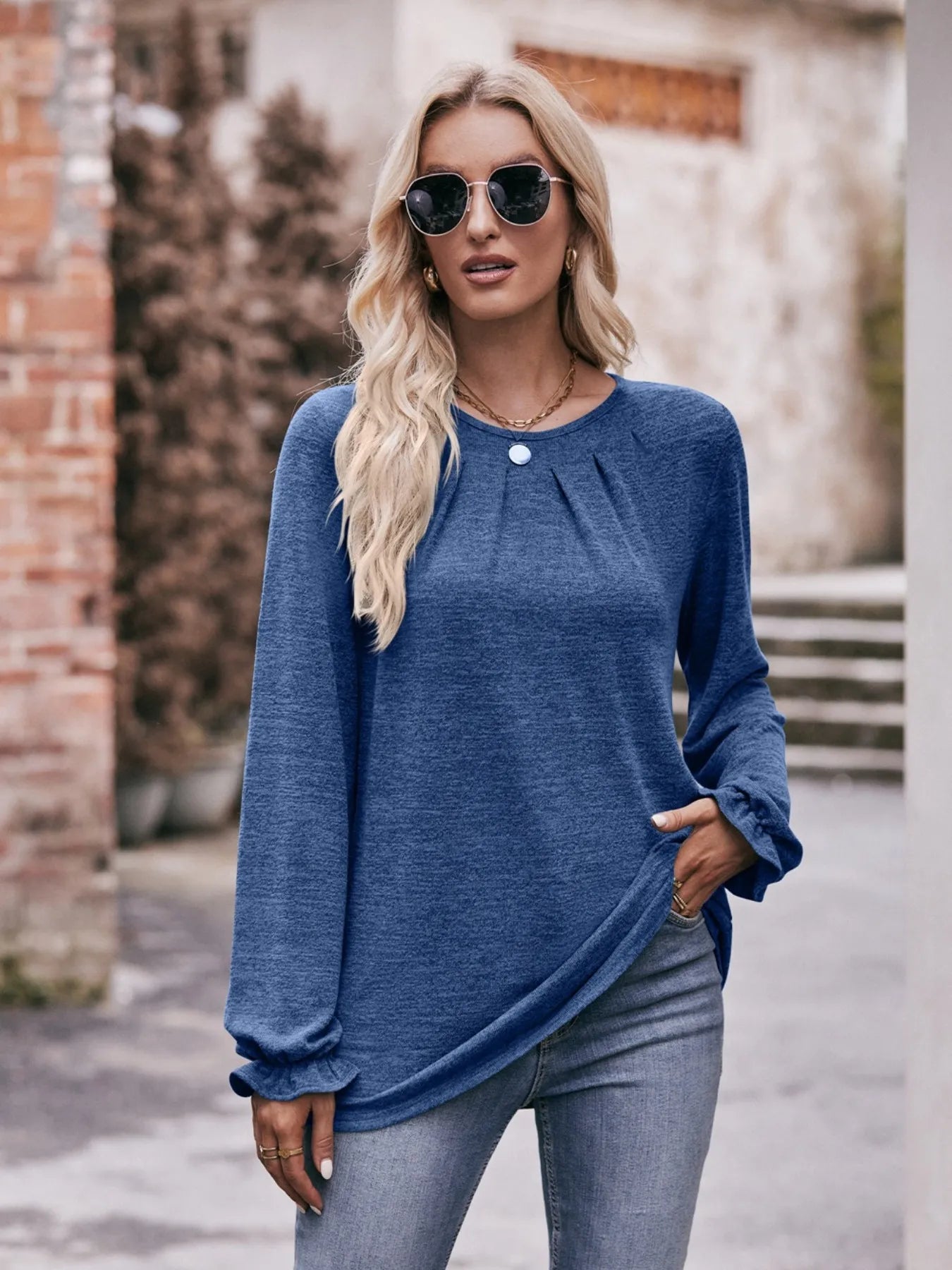 Woman wearing a blue long-sleeve top and sunglasses outdoors.