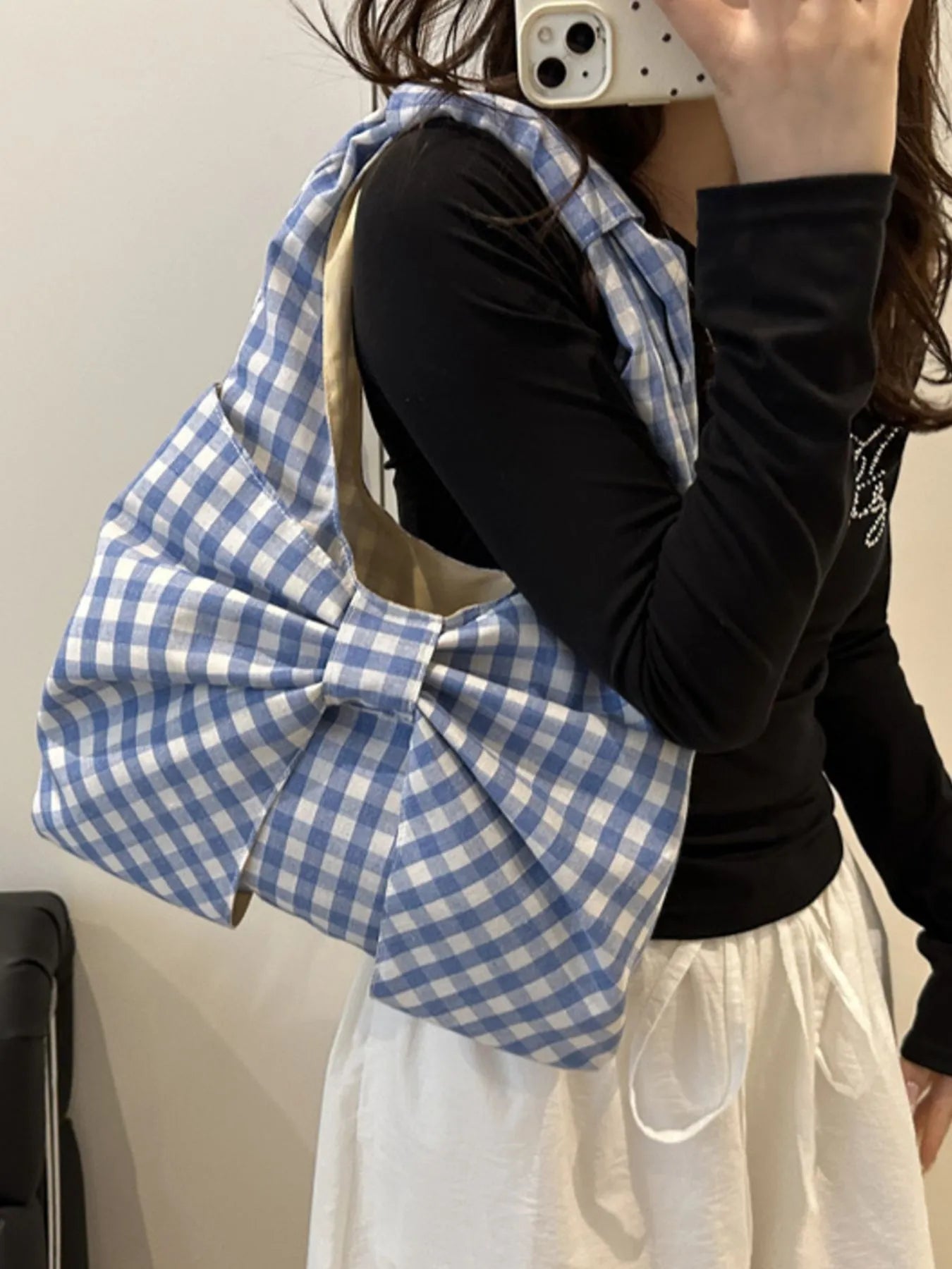 Person holding a blue and white checkered bag with a bow, wearing a black top and white skirt.