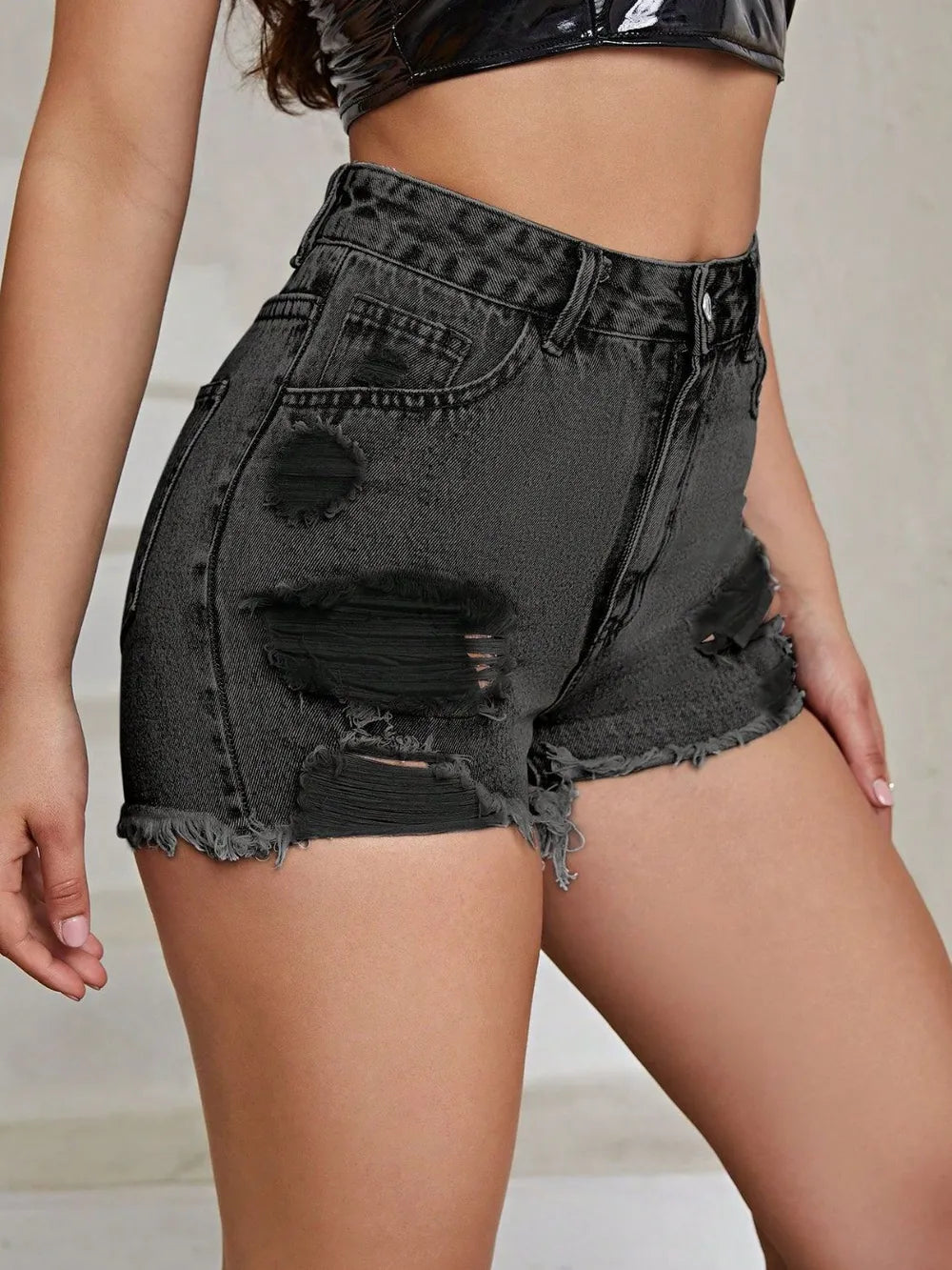 Black distressed denim shorts worn by a person on a neutral background
