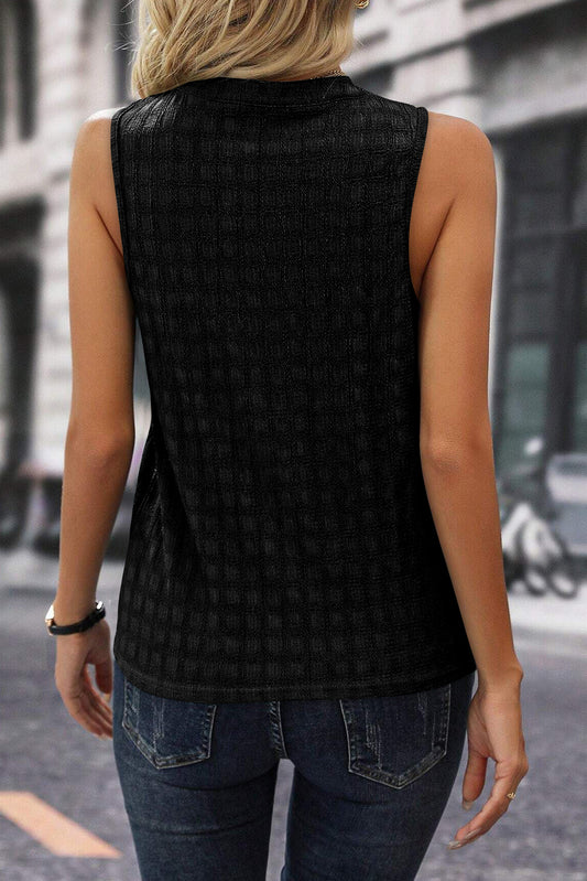 Person wearing a black sleeveless top with a textured pattern, standing on a street.