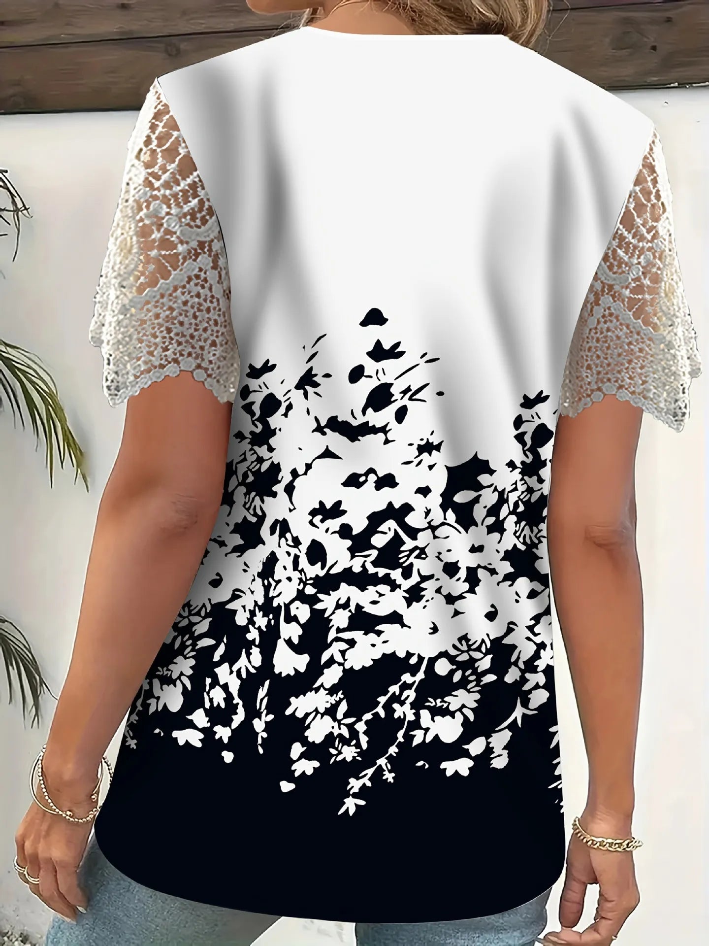 White top with black floral design and lace sleeves on a neutral background
