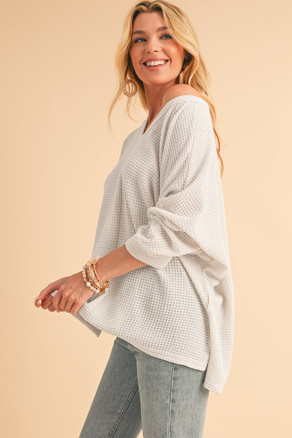 Woman wearing a light gray oversized sweater and jeans on a beige background