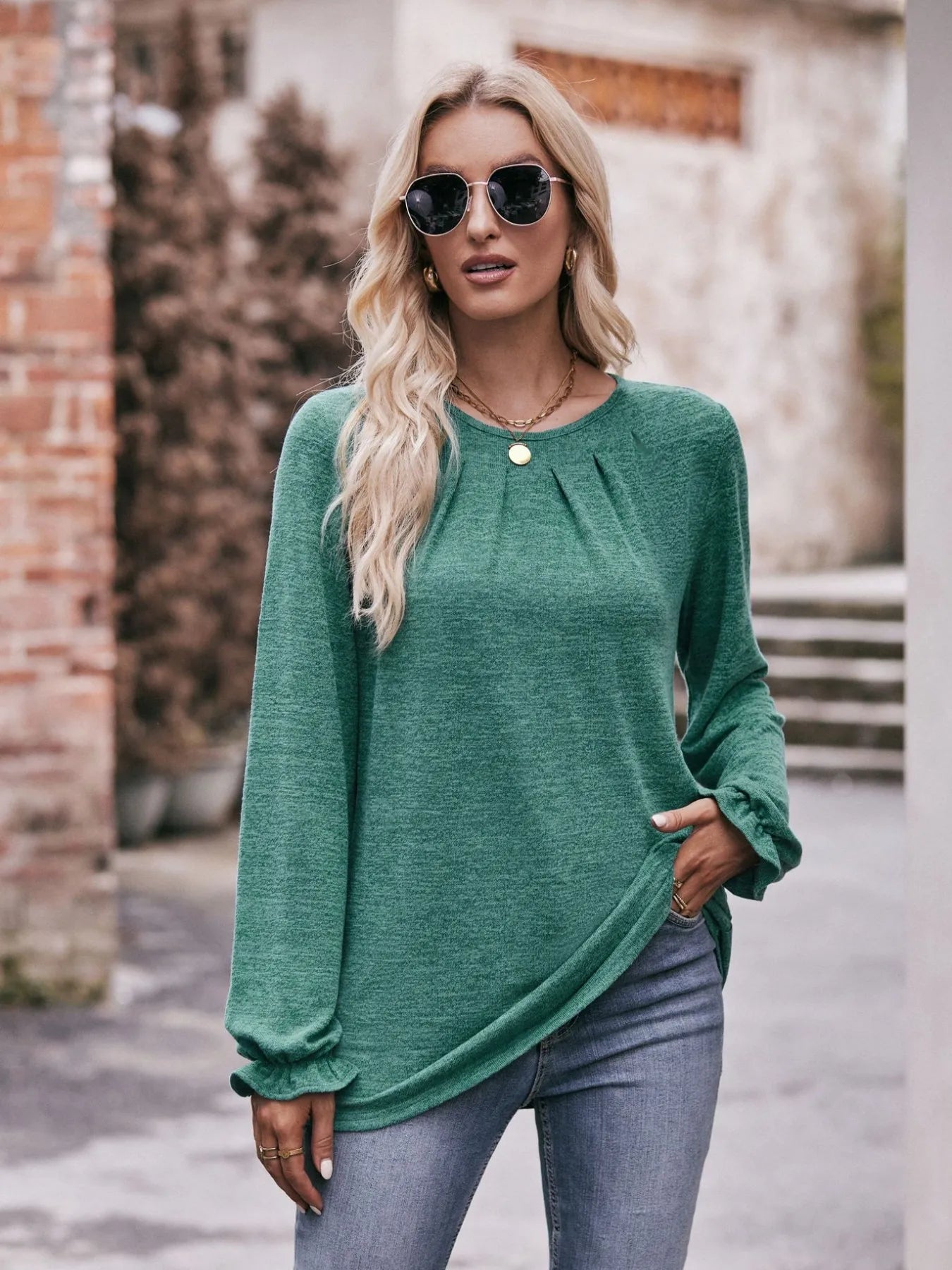 Woman wearing a green long-sleeve top and sunglasses outdoors.