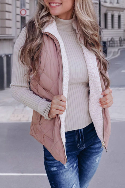 Woman wearing a light pink quilted vest over a beige sweater with blue jeans on a city street.