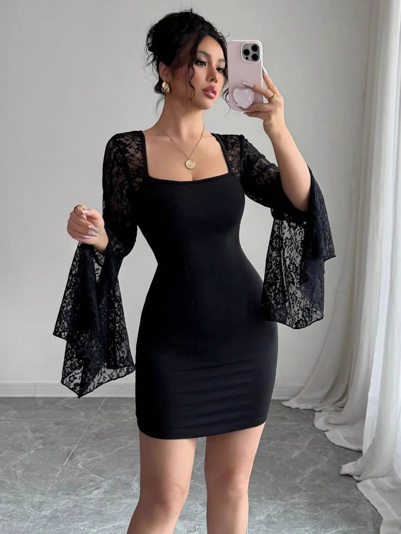 Woman taking a mirror selfie wearing a black dress with lace sleeves in a room.