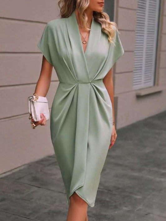 Woman wearing a light green dress holding a white clutch against a neutral background