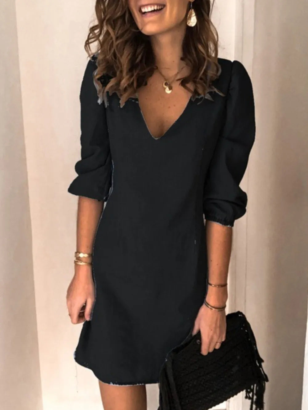 Woman wearing a black dress holding a black clutch against a neutral background