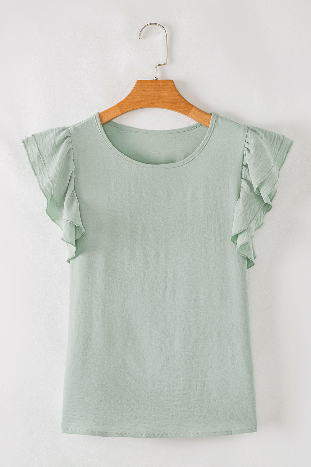 Green top with ruffled sleeves on a wooden hanger against a white background