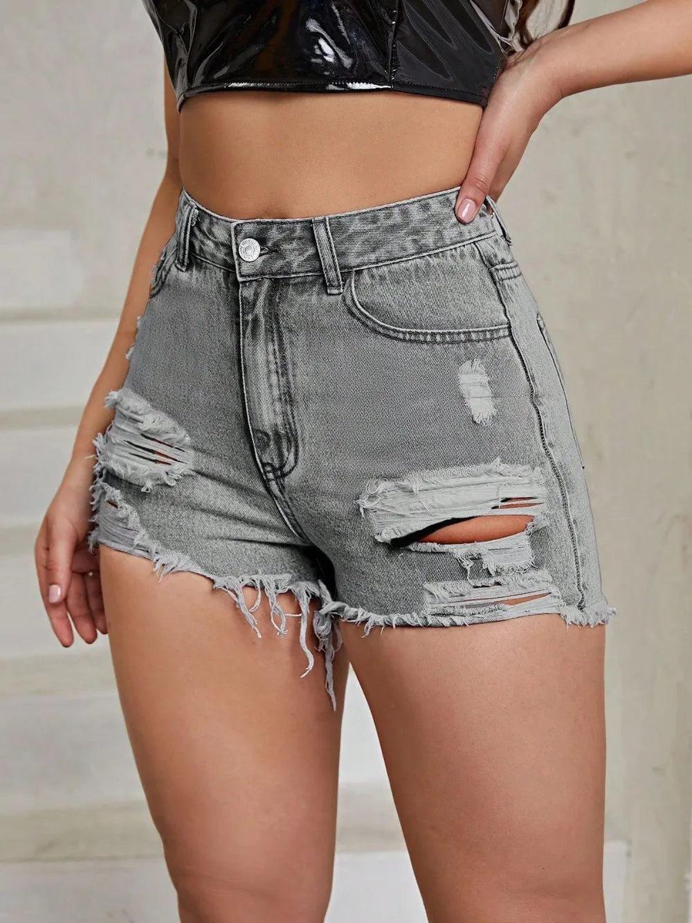 Person wearing distressed gray denim shorts with a plain background