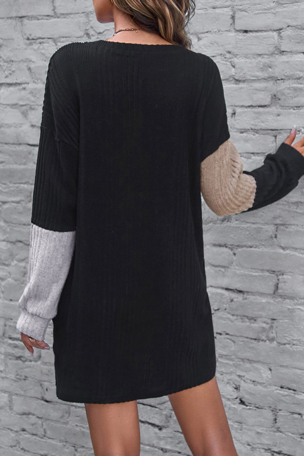 Black dress with color-blocked sleeves against a stone wall background