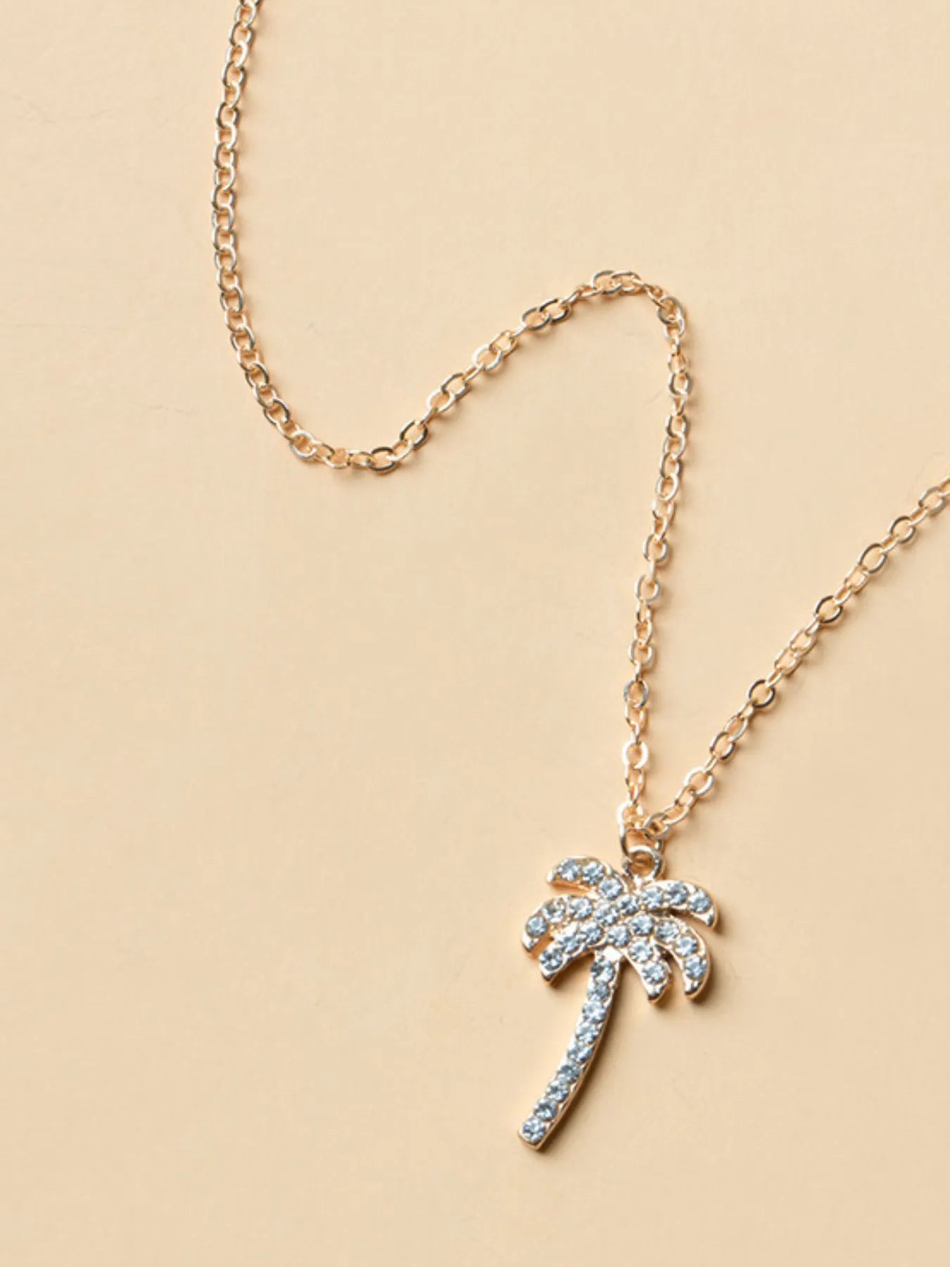 Gold necklace with a palm tree pendant on a beige background