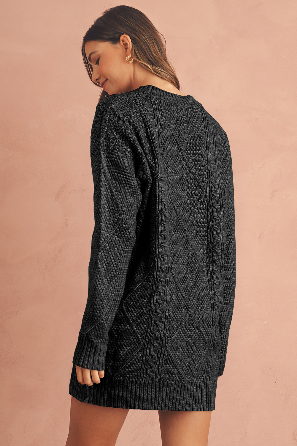 Woman wearing a dark gray cable knit sweater against a pink background