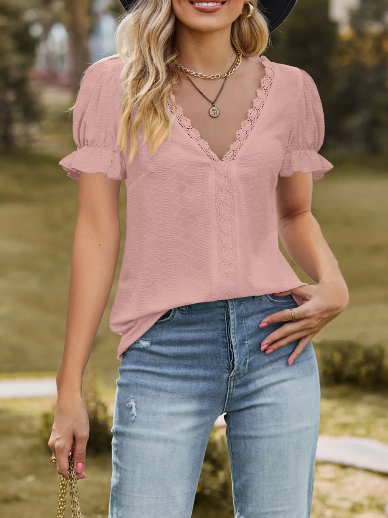 Woman wearing a pink blouse with lace details and blue jeans outdoors.